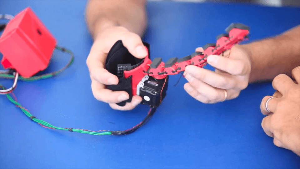 Hands demonstrating a flexible red robotic finger prototype